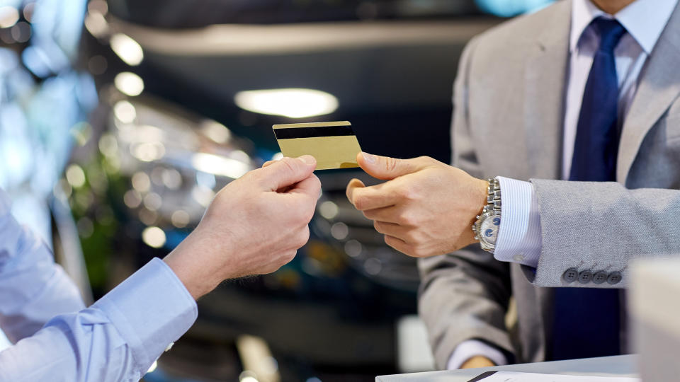 auto business, sale and people concept - close up of customer giving credit card to car dealer in auto show or salon.