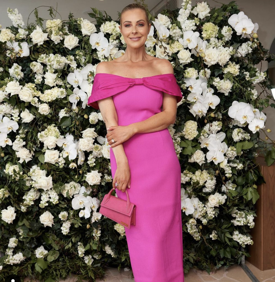 Lorinska poses in front of a floral wall in a pink gown.