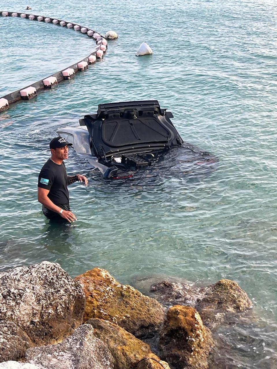 Un bombero de Cayo Hueso de pie en aguas poco profundas junto a un Dodge Challenger hundido que, según la policía, un hombre condujo hacia el océano el domingo 28 de abril de 2024. Key West Police Department