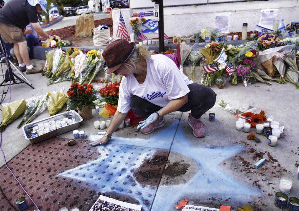 FILE - Elena Colombo chalks a Star of David amongst flowers and candles left at a makeshift shrine placed at the scene of a Sunday confrontation that lead to death of a demonstrator Tuesday, Nov. 7, 2023, in Thousand Oaks, Calif. California authorities have arrested a man in connection with the death of a Jewish protester during demonstrations over the Israel-Hamas war. (AP Photo/Richard Vogel, File)