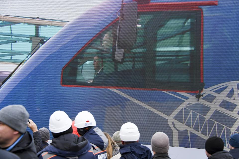People watch a giant TV screen with Russian President Vladimir Putin, behind a window, riding a train across a bridge linking Russia and the Crimean peninsula in Taman, Russia, Monday, Dec. 23, 2019. Putin on Monday inaugurated a railway bridge to Crimea, the longest in Europe, which is intended to facilitate links with Crimea, which Russia annexed from Ukraine in 2014. (AP Photo)