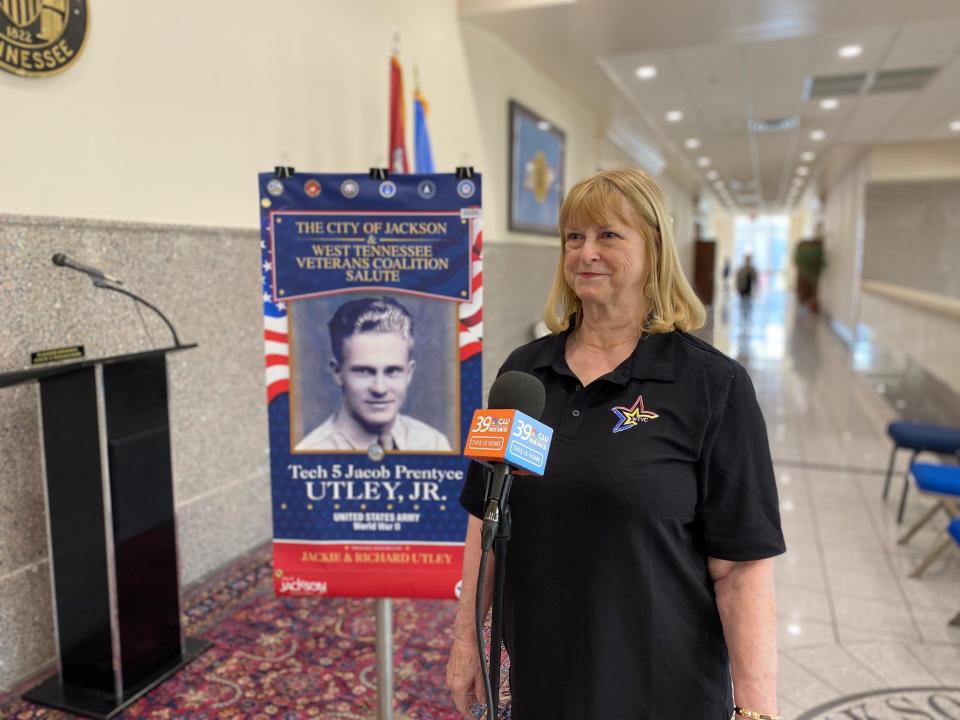 Jackie Utley, chair of the West Tennessee Veterans Coalition, stands in front of the first banner of the project, which depicts her father, Tech 5 Jacob Prentyce Utley Jr.