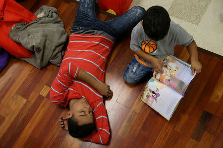 FILE PHOTO: After being detained and released by law enforcement, an undocumented immigrant from Honduras and his son pass the time before beginning a bus journey to Louisiana at the Catholic Charities relief center in McAllen, Texas, U.S., April 6, 2018. REUTERS/Loren Elliott/File Photo