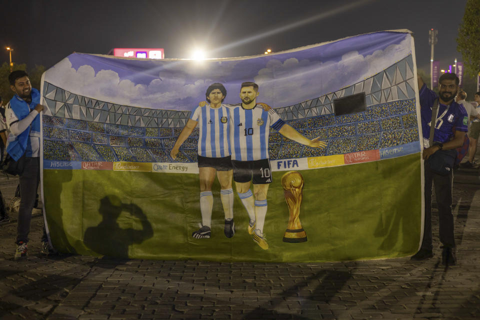 Mohid Data and Aayush Verma from India show a huge painting of their heroes, Lionel Messi and Diego Maradona with the World Cup trophy, prior to the World Cup group C soccer match between Poland and Argentina at the Stadium 974 in Doha, Qatar, Wednesday, Dec. 30, 2022. (AP Photo/Ciaran Fahey)