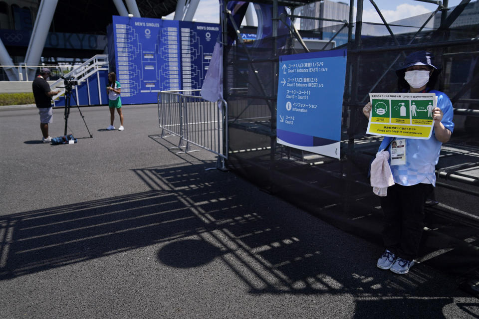 A volunteer holds a sign warning people to keep their distance and wash their hands during the first round of the tennis competion at the 2020 Summer Olympics, Saturday, July 24, 2021, in Tokyo, Japan. (AP Photo/Seth Wenig)