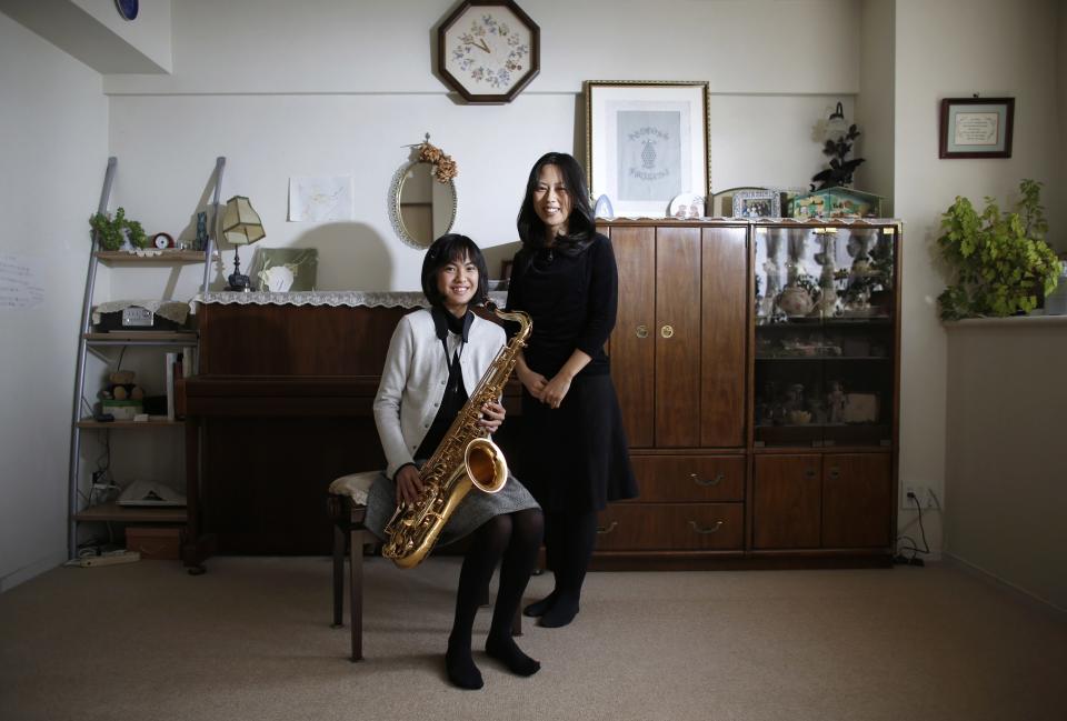 Manami Miyazaki and her daughter Nanaha, holding her alto saxophone, pose for a portrait in the living room of their home in Tokyo