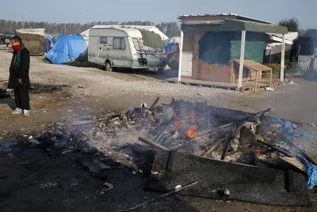 A migrant stands next to a burning makeshift shelter on the second day of their evacuation and transfer to reception centers in France, during the dismantlement of the camp called the "Jungle" in Calais, France, October 25, 2016. REUTERS/Pascal Rossignol