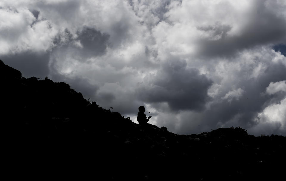 In this photo taken Wednesday, Dec. 5, 2018, a young boy who scavenges for recyclable materials for a living throws a rock in the air to pass the time as he takes a break while sitting on top of a mountain of garbage at the dump in the Dandora slum of Nairobi, Kenya. As the world meets again to tackle the growing threat of climate change, how the continent tackles the growing solid waste produced by its more than 1.2 billion residents, many of them eager consumers in growing economies, is a major question in the fight against climate change. (AP Photo/Ben Curtis)