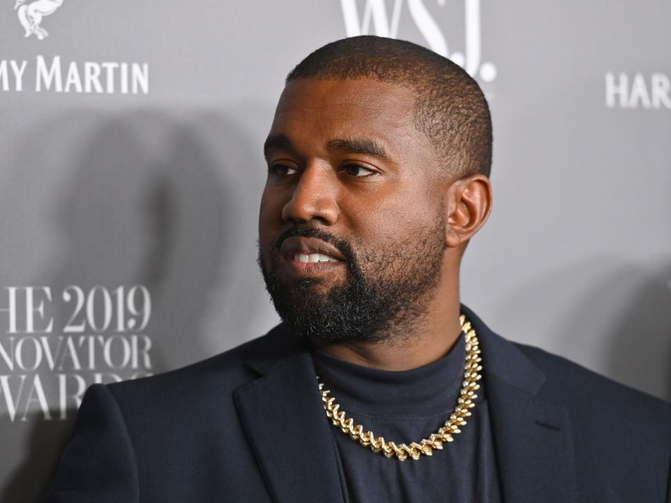 Kanye West looks off camera while wearing black jacket and gold chain at WSJ red carpet event
