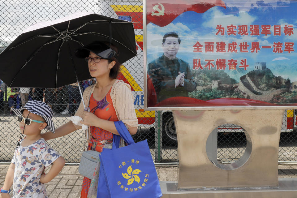 FILE - In this June 30, 2019, file photo, visitors walk past a poster featuring Chinese President Xi Jinping during an open day of Stonecutter Island naval base, in Hong Kong to mark the 22nd anniversary of Hong Kong handover to China. China’s central government has dismissed Hong Kong pro-democracy protesters as clowns and criminals while bemoaning growing violence surrounding the monthslong demonstrations.(AP Photo/Kin Cheung, File)