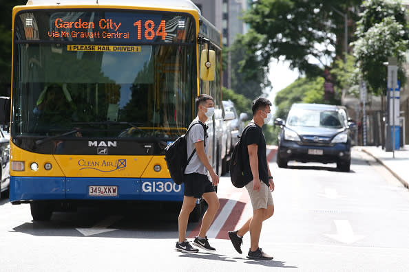 People wearing masks walk through the Brisbane CBD in front of a bus.