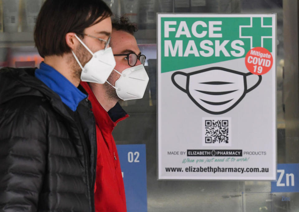 People wearing face masks walk past a sign advertising masks in Melbourne.