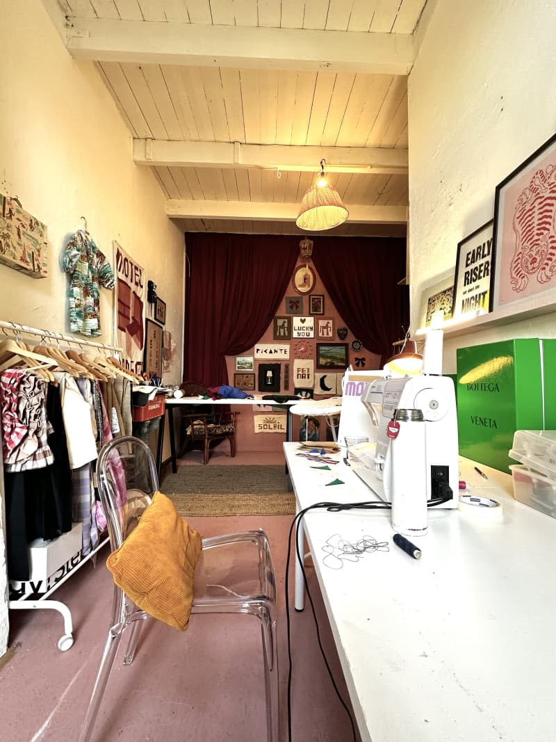 Attic sewing room with ping wall full of hanging art with red velvet curtains.