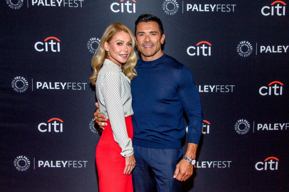 the couple posing at PaleyFest; Kelly in a polka dot top with a skirt, Mark in a sweater and slacks