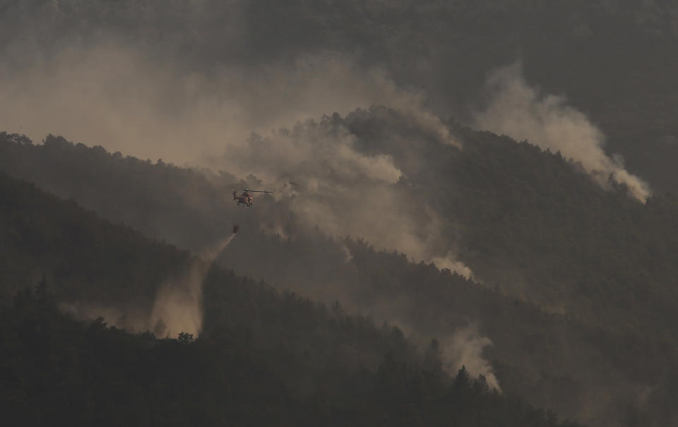 A firefighting helicopter pours water onto a wildfire in northern Athens, Saturday, Aug. 7, 2021. Wildfires rampaged through Greek forests for yet another day Saturday, threatening homes and triggering more evacuations a day after hundreds of people were plucked off beaches by ferries in a dramatic overnight rescue. (AP Photo/Lefteris Pitarakis)