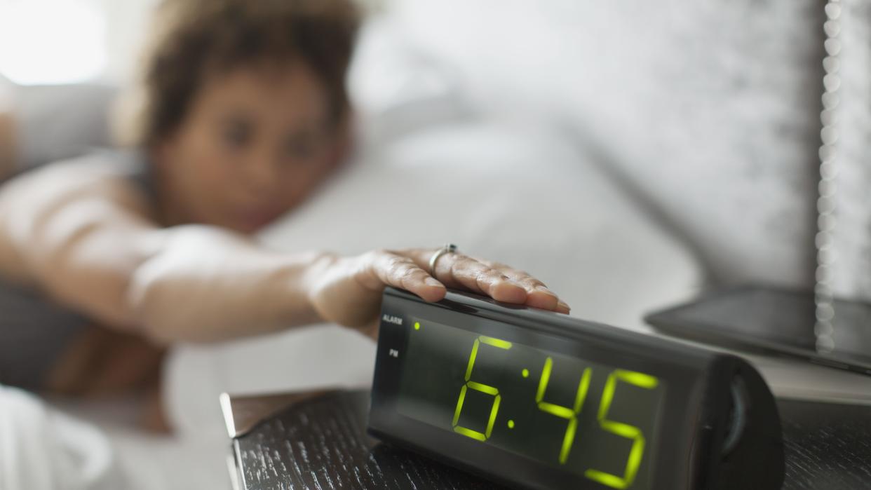 person in bed hitting alarm clock early in the morning