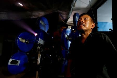 A villager sits next to a projector showing a film, during a circumcision party in Rempoa village on the outskirts of Jakarta, Indonesia, April 9, 2017. REUTERS/Beawiharta/Files