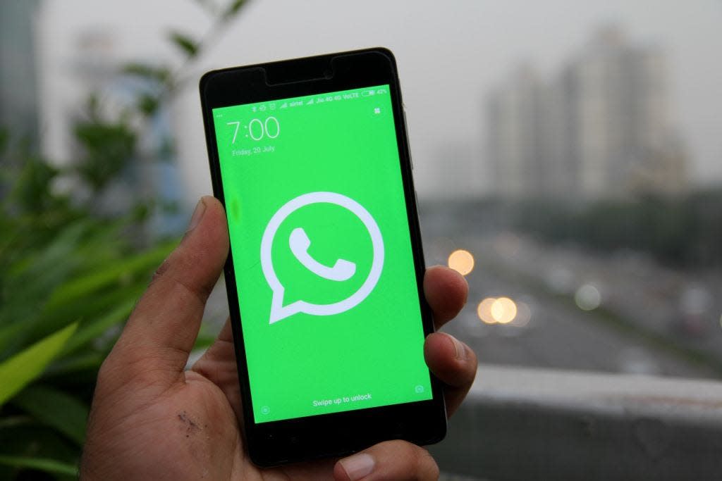 A hand holds a mobile phone displaying the green-and-white WhatsApp logo