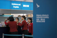 In this March 26, 2019 photo, staff members chat at the check-in counter of Cathay Pacific Airways at the Hong Kong International Airport. Cathay Pacific Airways is acquiring Hong Kong-based budget airline HK Express. Cathay said Wednesday, March 27, 2019, it will pay 4.93 billion Hong Kong dollars ($628 million) for HK Express. It said the acquisition will retain its identity as a separate brand and be operated as a low-cost carrier. (AP Photo/Kin Cheung)