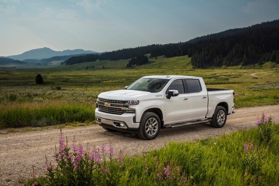 A white Chevy Silverado driving on a road, with a green field in the background