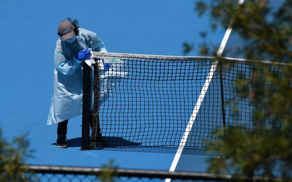 People wearing personal protective equipment are seen disinfecting a tennis court after a training session at Melbourne Park - JAMES ROSS/EPA-EFE/Shutterstock