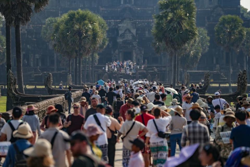 Large crowd of tourists exploring the ancient Angkor Wat temple, bordered by palm trees, in Cambodia