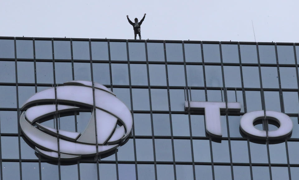 French urban climber Alain Robert, well known as "Spiderman", raises his arms as he finished to climb the Total tower in the Paris business district of La Defense, Monday, Jan 13, 2020, in support of the transport strikes. (AP Photo/Michel Euler)