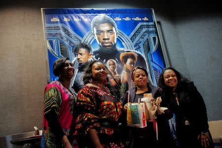 A group of women pose for a photo in front of a poster advertising the film "Black Panther" on its opening night of screenings at the AMC Magic Johnson Harlem 9 cinemas in Manhattan. REUTERS/Andrew Kelly