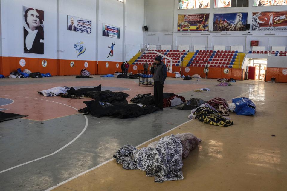 A man speaks on his cellphone among bodies, victims of the earthquake, at an indoor stadium, in Kahramanmaras, southeastern Turkey, Thursday, Feb. 9, 2023. Tens of thousands of people who lost their homes in a catastrophic earthquake huddled around campfires in the bitter cold and clamored for food and water Thursday, three days after the temblor hit Turkey and Syria. (AP Photo/Petros Giannakouris)