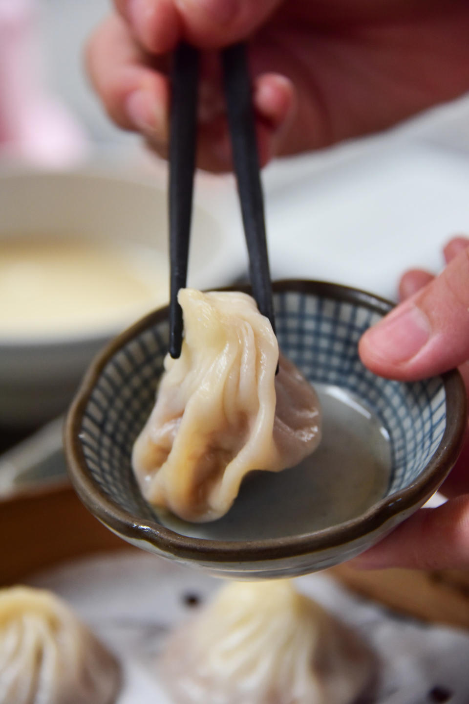 Close up of a pair of chopsticks holding a Chinese soup dumpling.