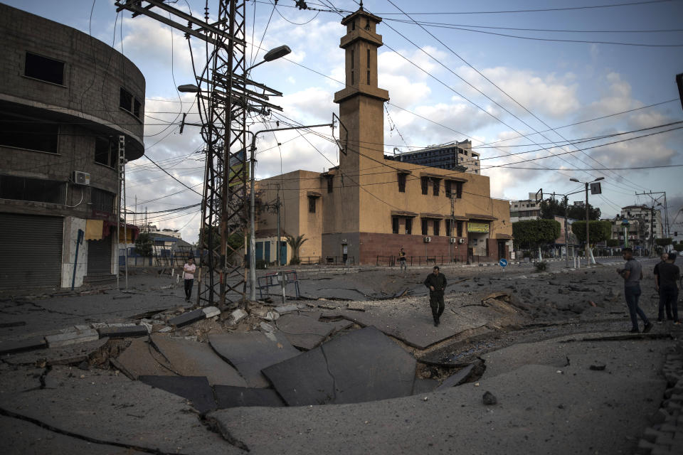 Palestinos caminando por una carretera destruida tras ataques aéreos en Ciudad de Gaza, el jueves 13 de mayo de 2021. (AP Foto/Khalil Hamra)