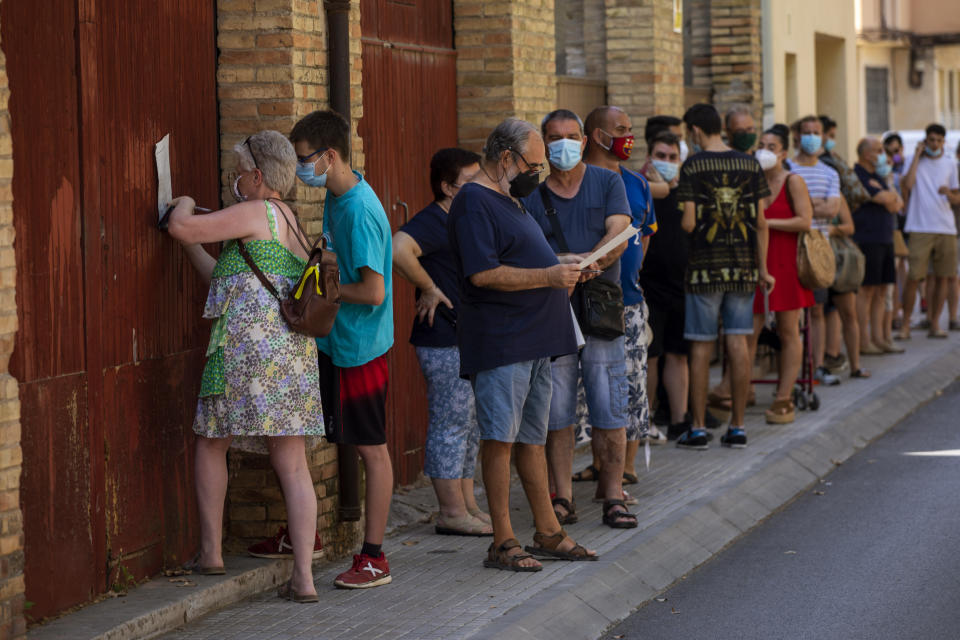 People wearing face masks queue up to be tested for COVID-19, at Vilafranca del Penedes in the Barcelona province, Spain, Monday, Aug. 10, 2020. Spain is facing another surge in coronavirus infections not even two months after beating back the first wave. (AP Photo/Emilio Morenatti)