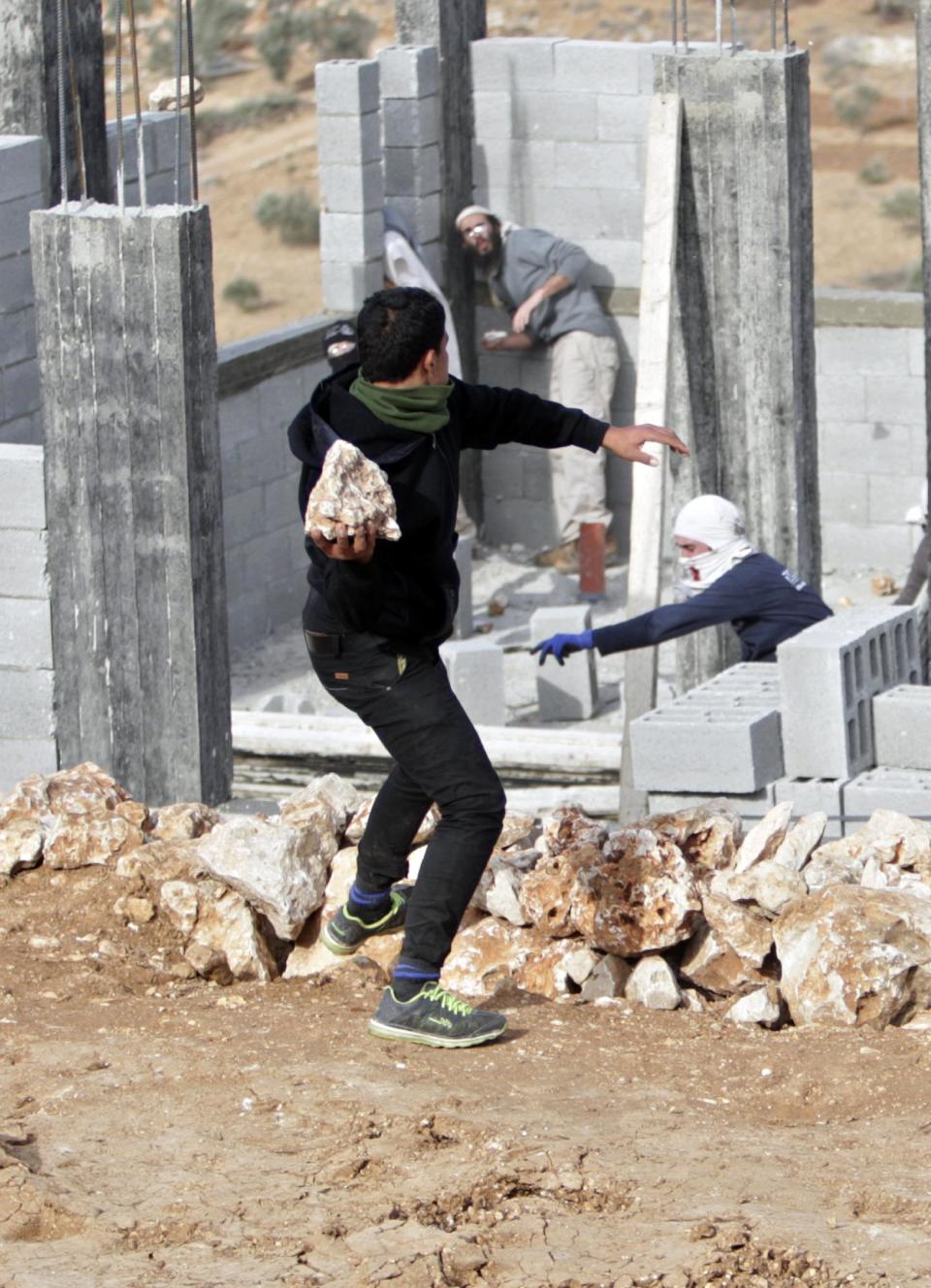 A Palestinian throws stones at Israeli settlers before they were detained by Palestinian villagers in a building under construction near the West Bank village of Qusra, southeast of the city of Nablus, Tuesday, Jan. 7, 2014. Palestinians held more than a dozen Israeli settlers for about two hours Tuesday in retaliation for the latest in a string of settler attacks on villages in the area, witnesses said. The military said the chain of events apparently began after Israeli authorities removed an illegally built structure in Esh Kodesh, a rogue Israeli settlement in the area. In recent years, militant settlers have often responded to any attempts by the Israeli military to remove parts of dozens of rogue settlements, or outposts, by attacking Palestinians and their property. The tactic, begun in 2008, is known as "price tag." (AP Photo/Nasser Ishtayeh)