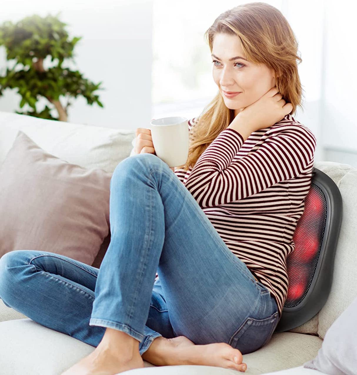 Woman sitting on a couch holding a mug while using a back massager.
