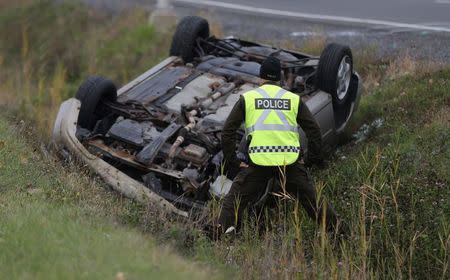 A Surete du Quebec (SQ) officer investigates an overturned vehicle in Saint-Jean-sur-Richelieu, Quebec October 20, 2014. REUTERS/Christinne Muschi