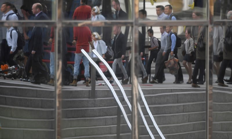 Workers are seen reflected in office windows as they cross London Bridge during the morning rush hour in London