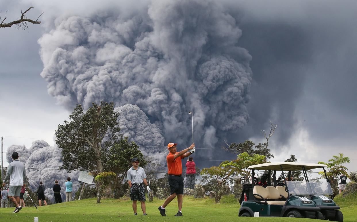 Goflers continue to play as an ash plume rises in the distance from the Kilauea volcano on Hawaii's Big Island on Tuesday. .  (Photo by Mario Tama/Getty Images)