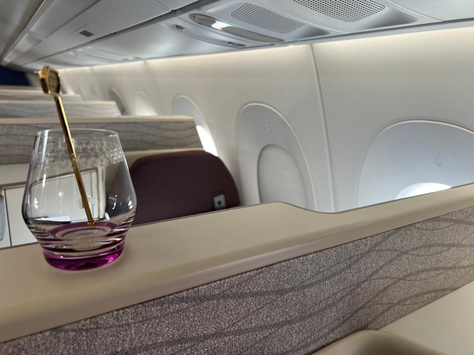 A glass sitting on the ledge between business class seats.