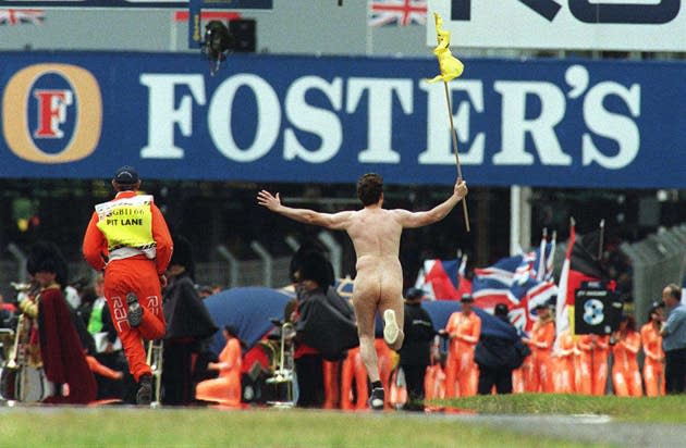 A pit lane marshal sets off in hot pursuit as a streaker sprints down the finishing straight ahead of the 1998 race. Michael Schumacher was the eventual winner, the first of three Silverstone successes