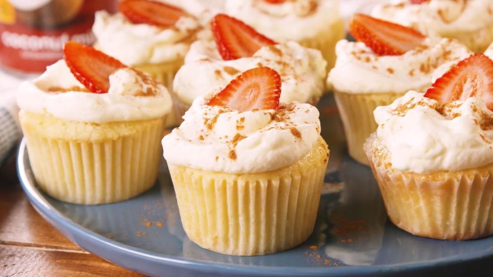 tres leches cupcakes with whipped cream and slices of strawberries