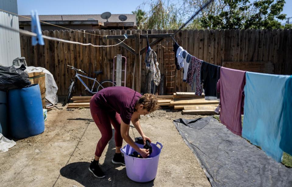 A woman takes laundry out of a bucket to hang on a line outside her trailer.