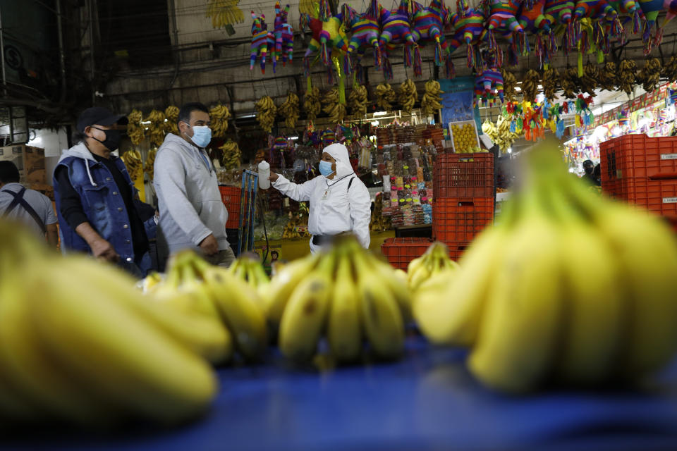 A worker wearing a protective suit offers antibacterial hand gel to passing shoppers and workers to curb the spread of the new coronavirus, inside the Central de Abastos, the capital's main market, in Mexico City, Tuesday, Dec. 8, 2020.(AP Photo/Rebecca Blackwell)