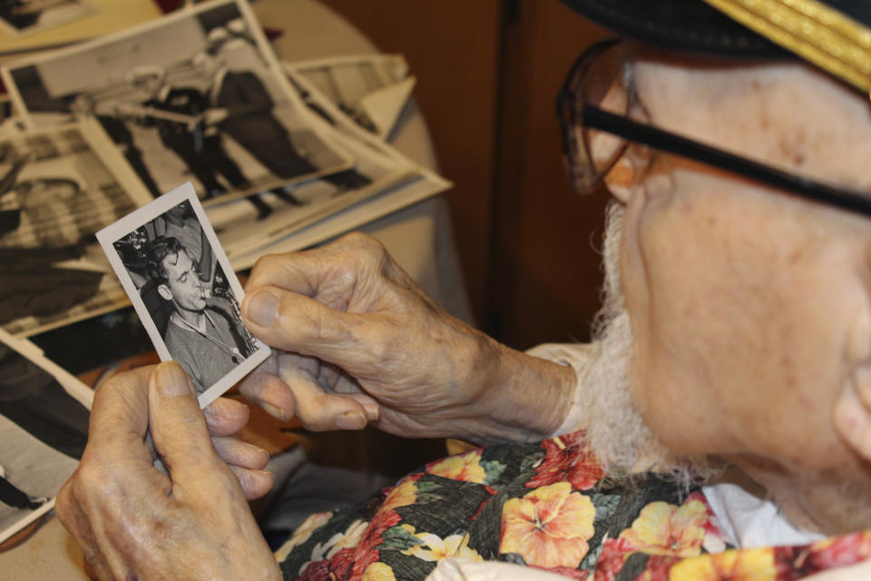 Pearl Harbor survivor Ira "Ike" Schab, 103, looks at an old photo of himself with a saxophone while sitting at the kitchen table in his home in Beaverton, Ore. on Monday, Nov. 20, 2023. Schab was in the U.S. Navy and played tuba in the Navy Band. Eighty-two years later, Schab plans to return to Pearl Harbor on the anniversary of the attack to remember the more than 2,300 servicemen killed. (AP Photo/Claire Rush)