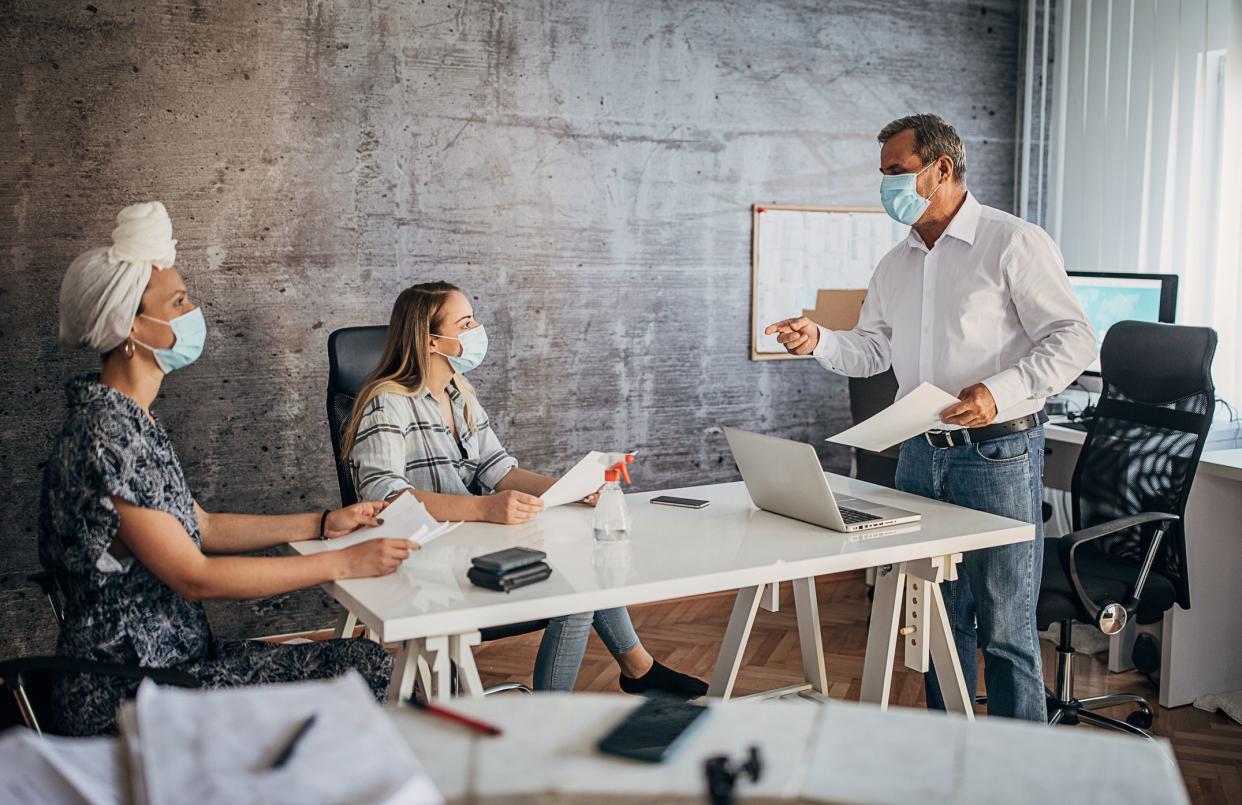 One senior man and two young women, diverse group of business people, with protective face masks having a meeting in the office.