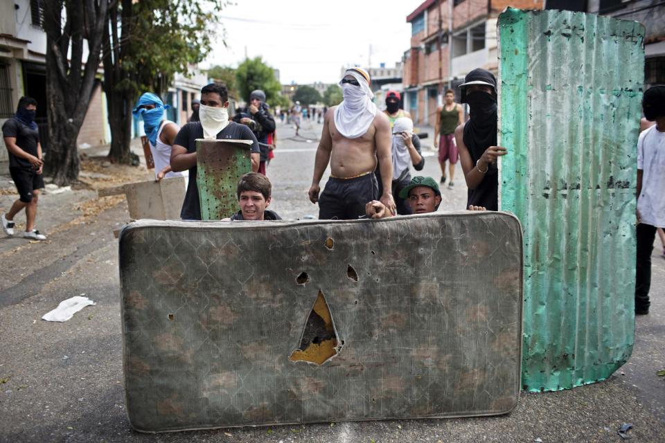 Opositores usan un colchón y un pedazo de aluminio para ocultarse, durante un enfrentamiento con la policía en la protesta contra el gobierno de Nicolás Maduro, en Valencia Venezuela, el miércoles 26 de febrero de 2014. Las protestas iniciaron con estudiantes en distintas ciudades, quienes están molestos por el crimen, los problemas económicos y la mano dura con la que la policía les ha respondido. (AP Photo/Rodrigo Abd)