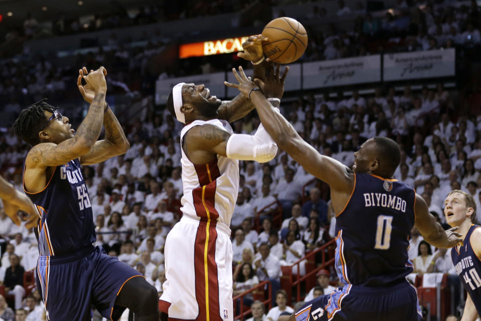 LeBron James, centro, del Heat de Miami, recibe falta de Bismack Biyombo (0), de los Bobcats de Charlotte, en la primera mitad del primer partido de la serie de primera ronda de los playoffs de NBA el domingo 20 de abril de 2014, en Miami. El Heat ganó 99-88 con 27 puntos de James. (AP Photo/Lynne Sladky)