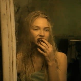 Sasha Luss reflecting in a mirror, looking concerned, with their hand on their mouth