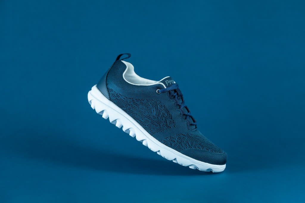 This is a photo of a Propét Travel Activ shoe photographed against a blue background. The shoe is also blue.