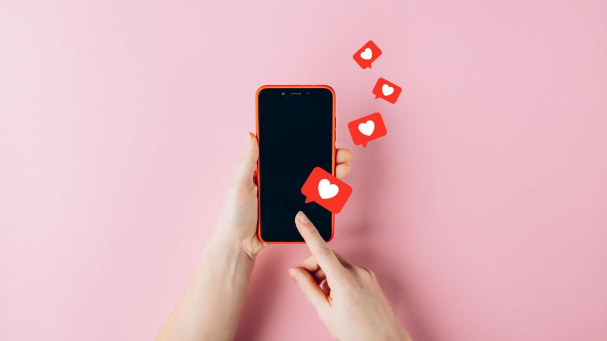 female hands holding red mobile phone with many social media likes on pink background