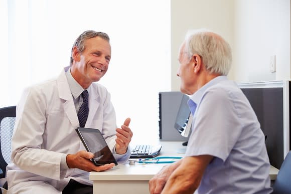 A doctor using a tablet to deliver positive test results to an elderly patient.